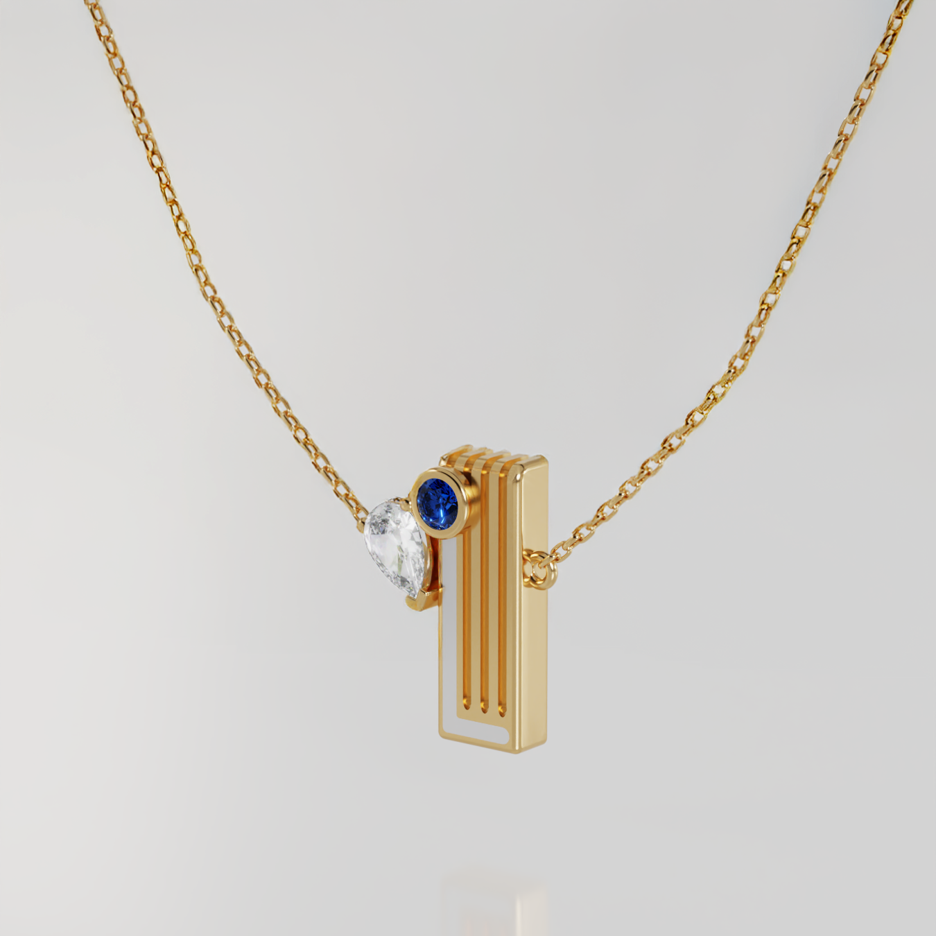 A gold pendant necklace featuring a vertical bar with a side round blue sapphire gemstone and a pear shaped white diamond, suspended from a delicate gold chain against a light gray background.