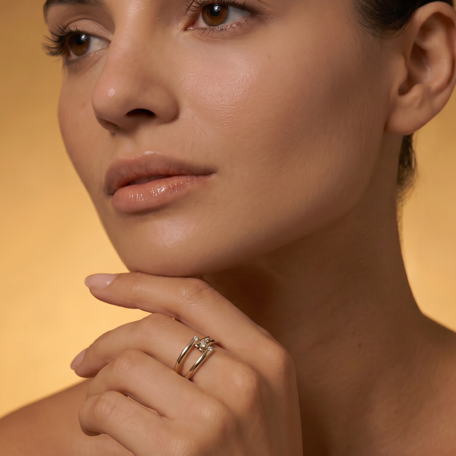 Close-up of a woman's face with a soft focus on her hand and yellow gold ring against a warm background