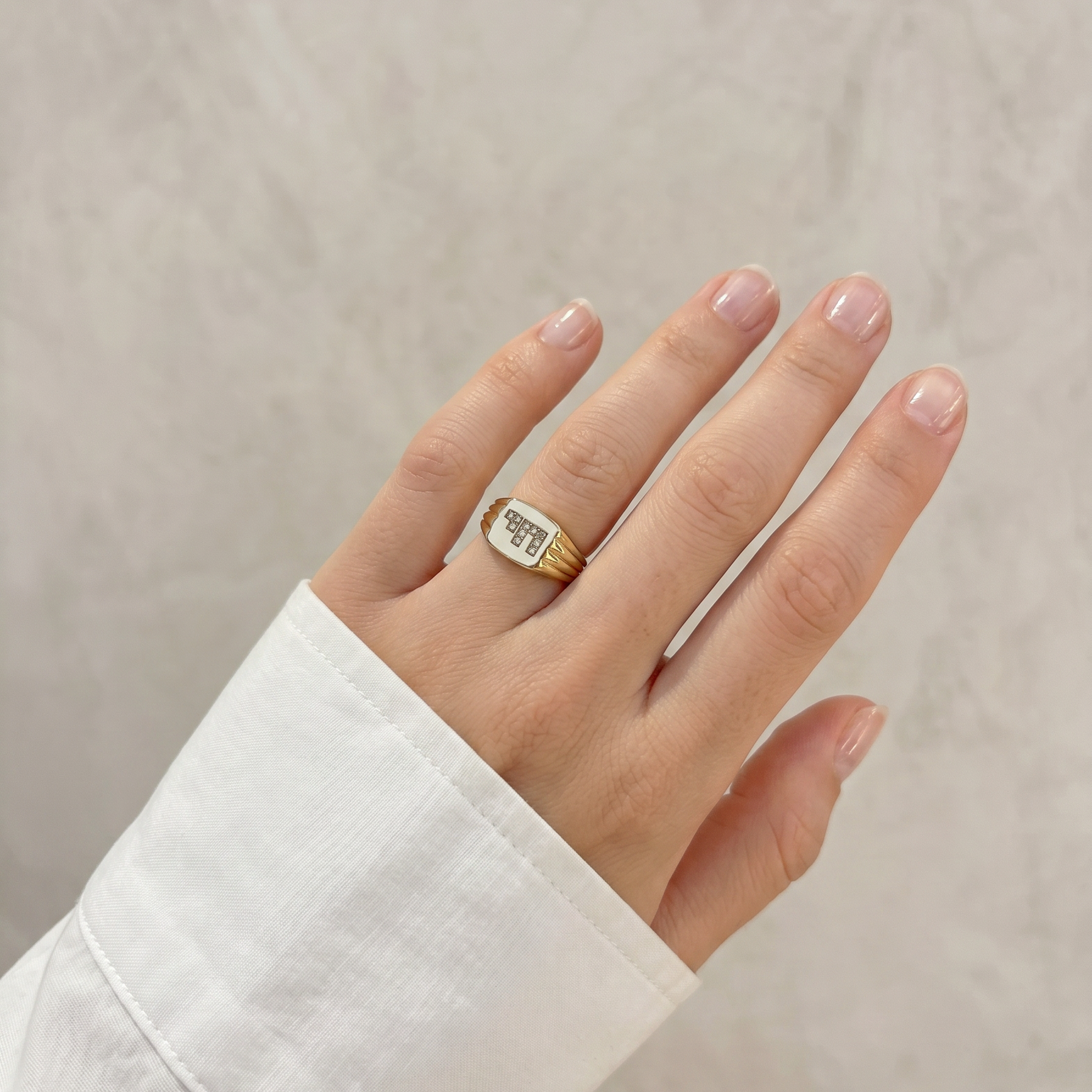 Gold signet ring with diamonds on ring finger with white sleeve