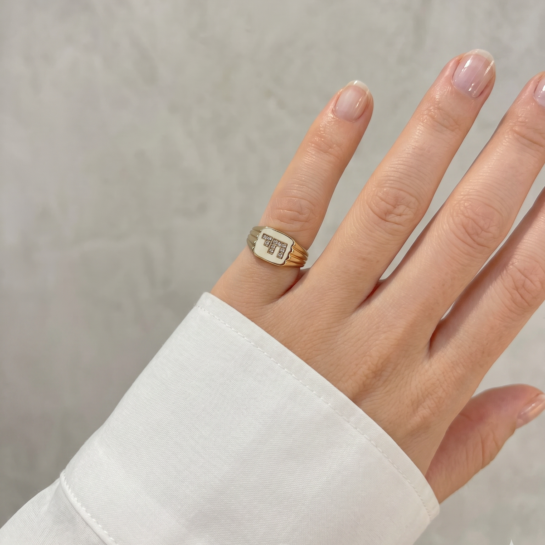 Gold signet ring with diamonds on pinky finger with white sleeve
