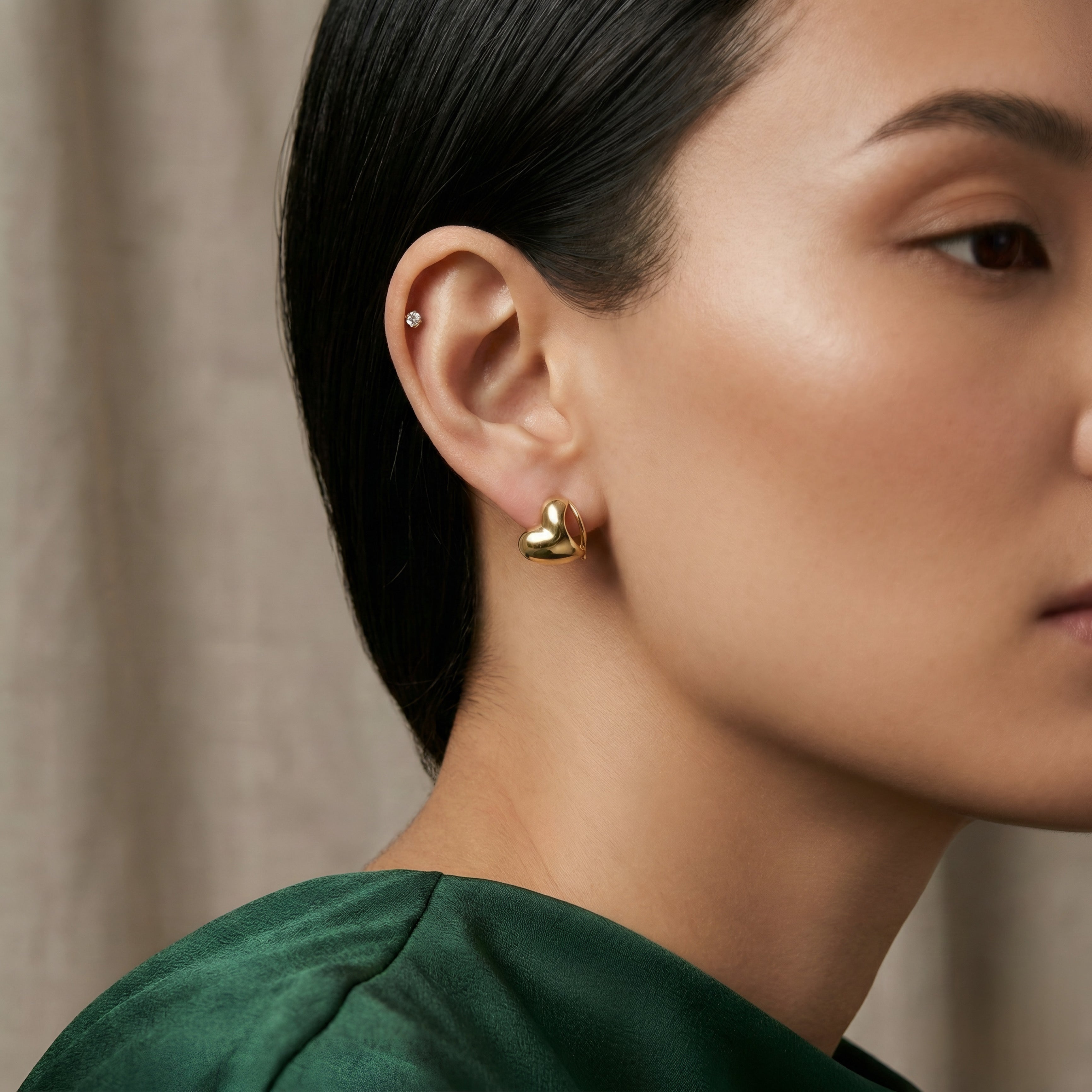 Close-up of a woman wearing gold heart-shaped earrings with a neutral background