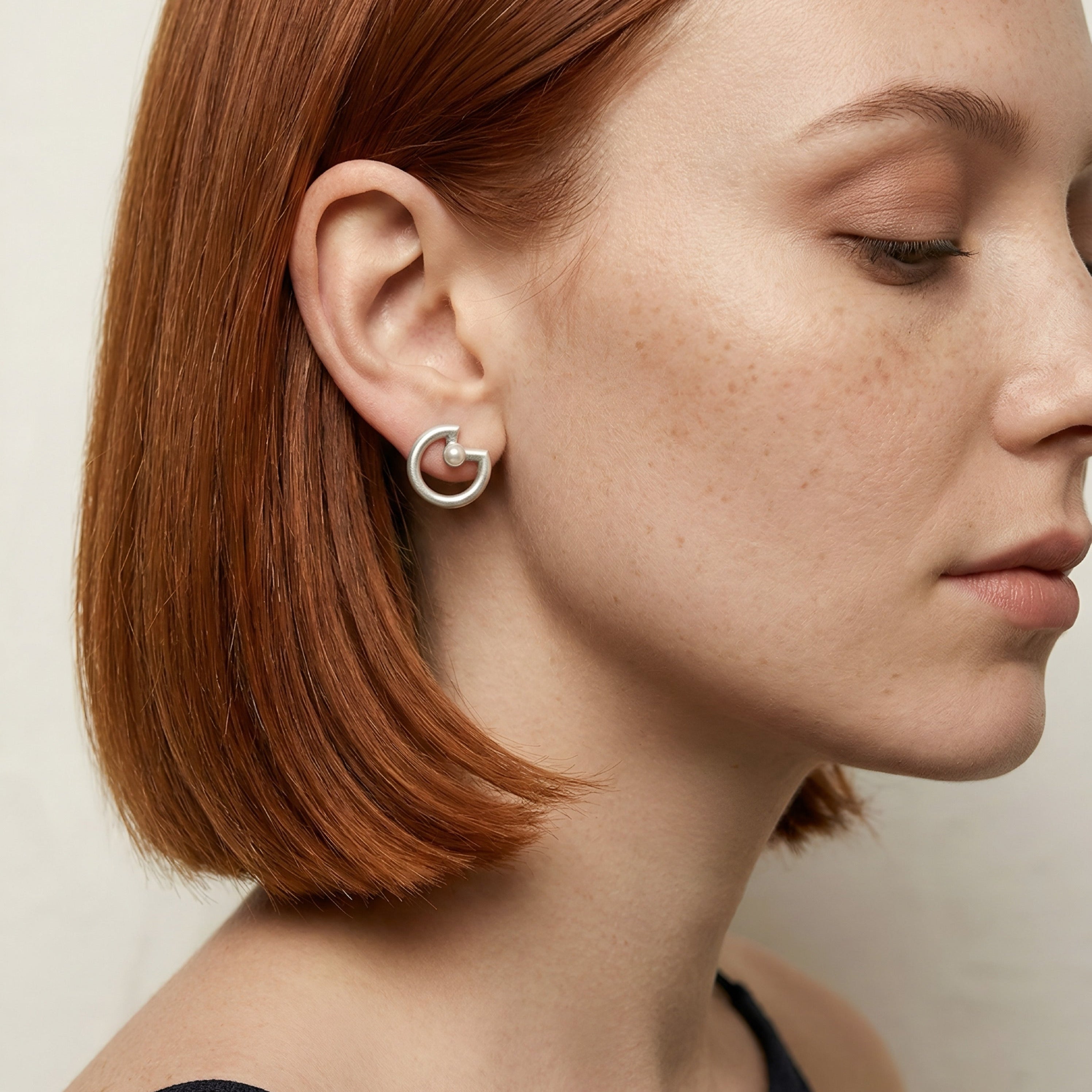 Close-up of a person wearing a silver earring with a circular design.