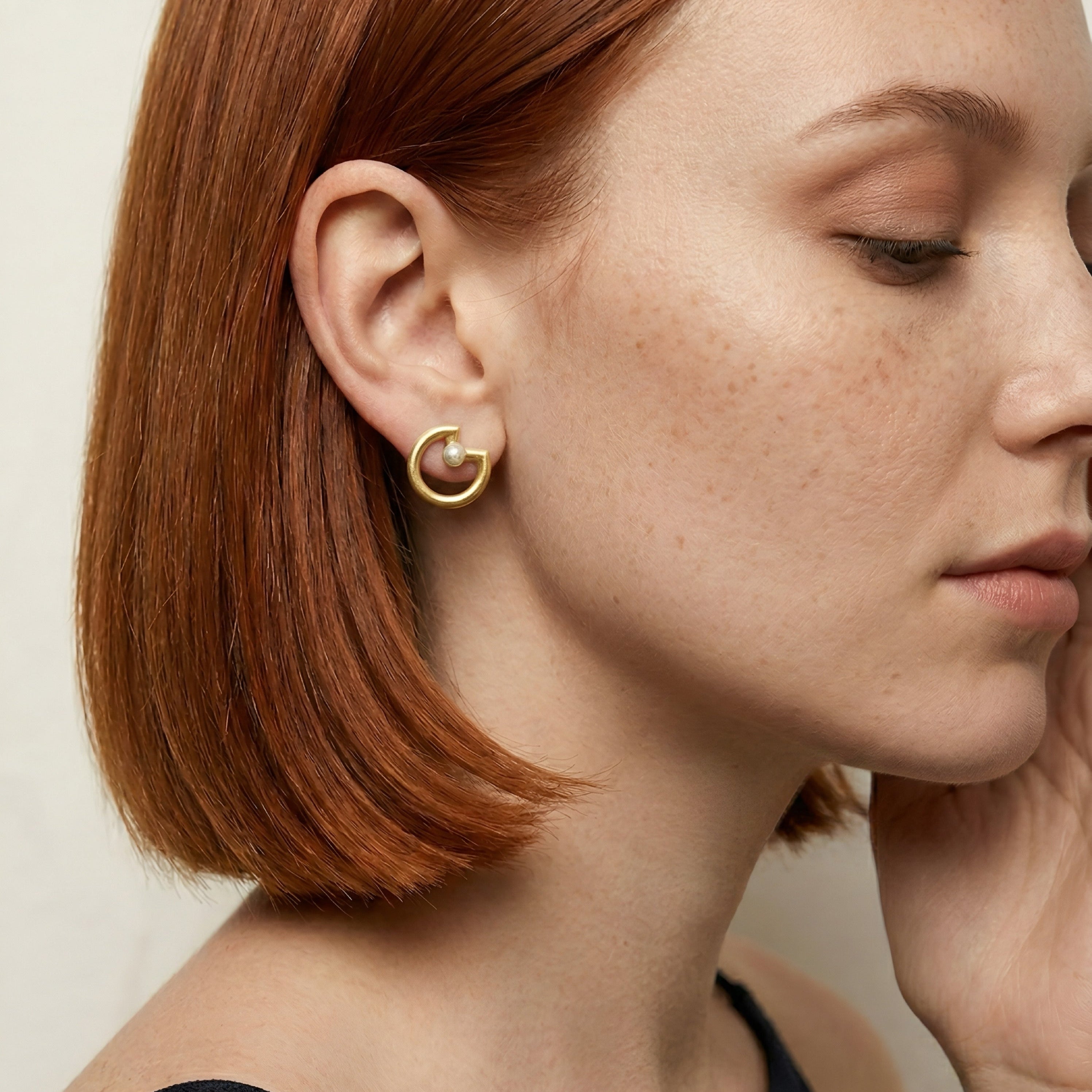 Woman with red hair wearing a gold earring against a neutral background