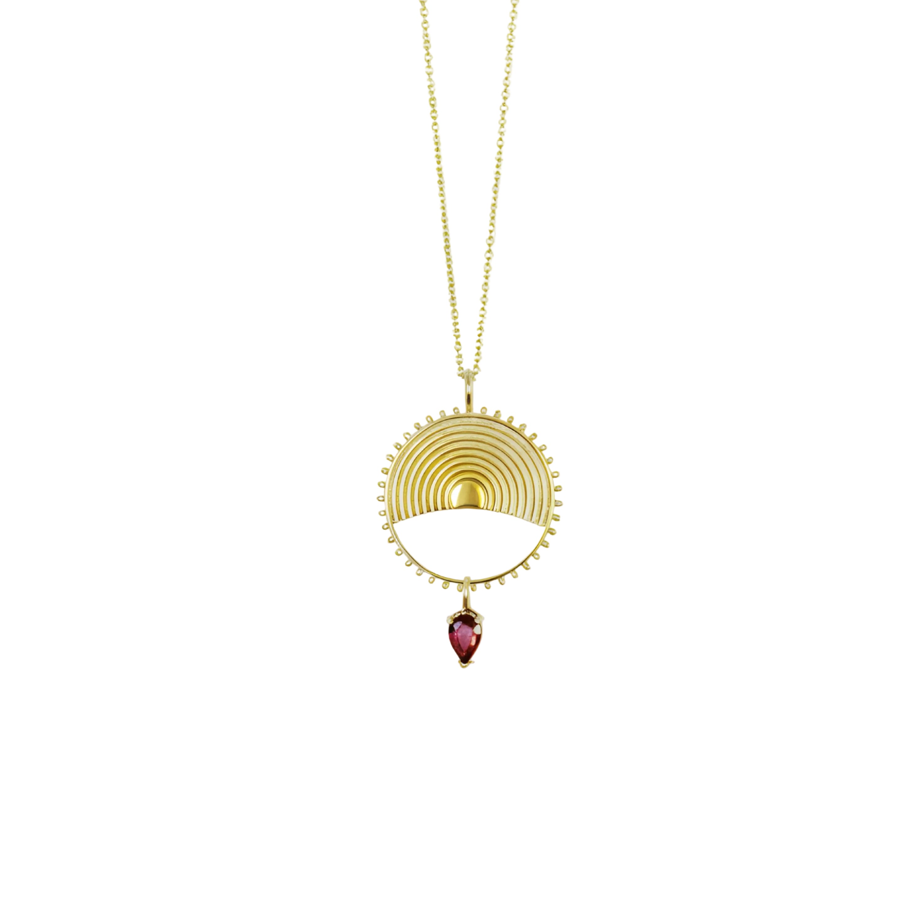 Gold necklace with a yellow gold circular pendant and gemstone on a white background