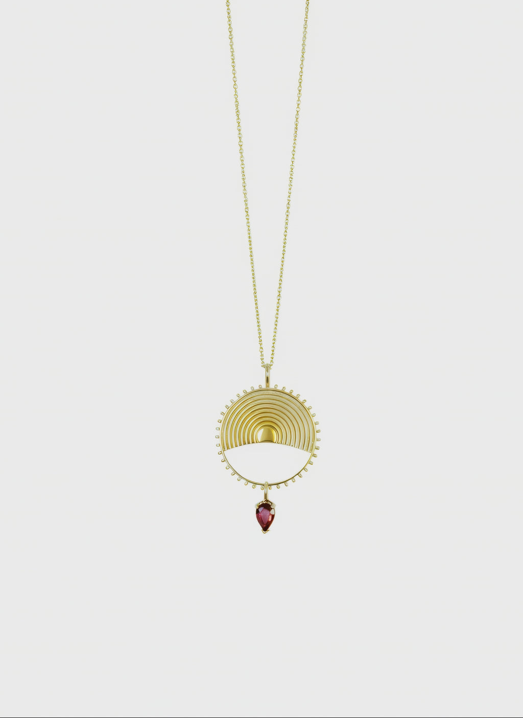 Gold necklace with a yellow gold circular pendant and gemstone on a white background